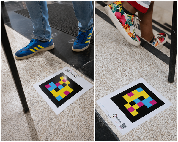 Side-by-side image of two NaviLens accessibility markers on terrazzo flooring inside a campus building. One person wears blue-and-yellow sneakers beside a marker near an entry mat, while another in floral sneakers stands beside a marker near stairs.