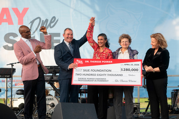 Five people on stage hold big check celebrating donation towards research