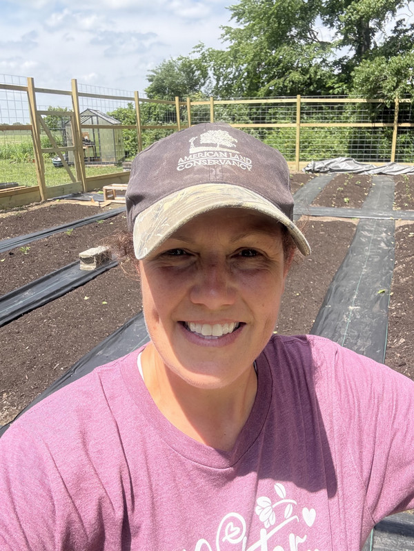 Selfie Photo of Sharie Craddock wearing cap and standing in front of farm bed
