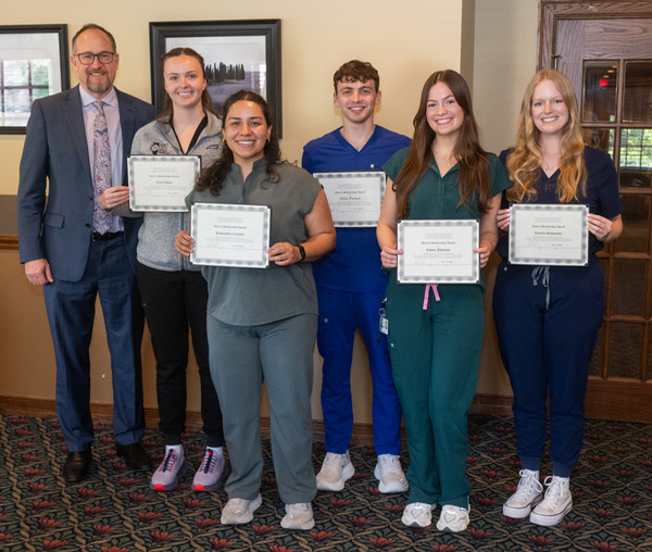 Students hold award plaques as they stand with Dean