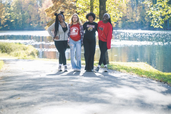 Four SIUE students pose standing for a photo under trees