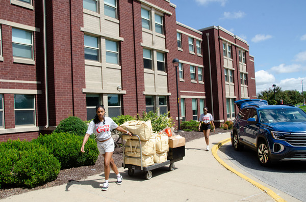 Exterior shot of two students moving in items walk across front of residence hall