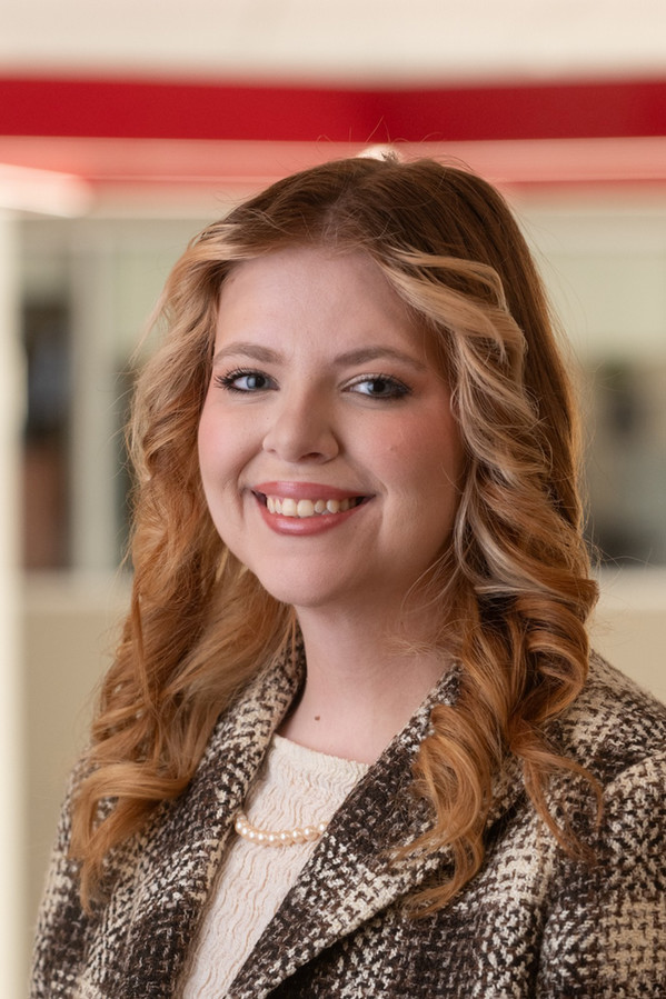 Caitlyn Heller smiles at the camera for a professional portrait, wearing a black-and-white patterned blazer, cream sweater and champagne pearl necklace.