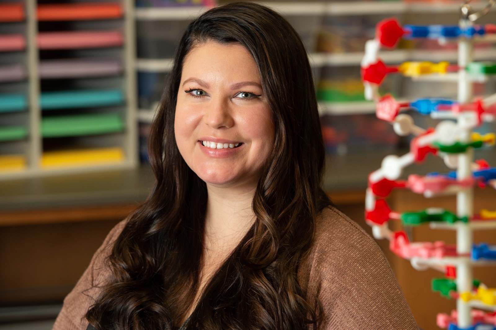 Portrait of Maurina Aranda indoors in front of a DNA apparatus and colorful classroom tools.