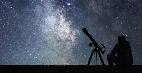 Night Sky with outline of person sitting by a telescope