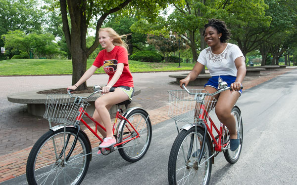 Two female students riding bicycles on campus