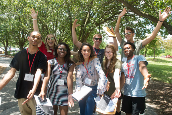 Group of students visiting campus standing outside with arms in the air