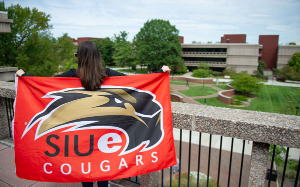 SIUE student with team flag above campus