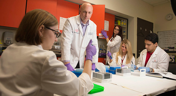 students in white coats conducting research in lab with professor