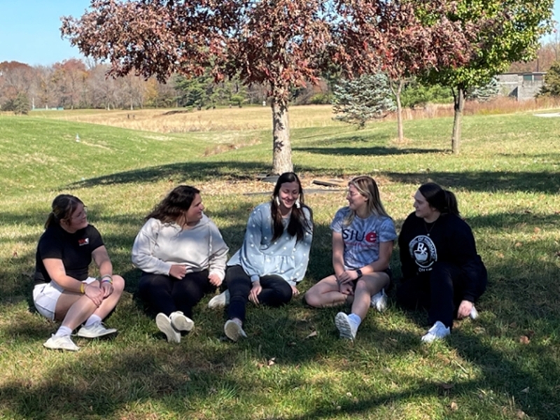 Students sitting in the grass outside in front of a garden talking